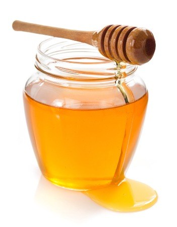 Large glass jar of honey, some spilling over the side, on a white isolated background. 